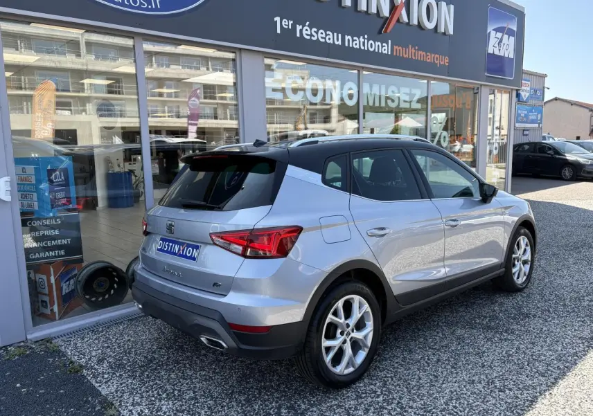 Vue 3/4 arrière droite d'une SEAT Arona 2024 gris clair avec jantes alliage et logo FR devant un showroom