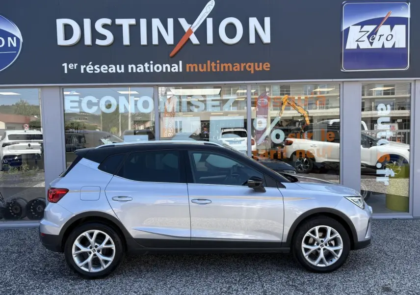 Profil latéral droit d'une SEAT Arona 2024 GRS avec toit noir et jantes alliage 16 pouces devant une vitrine Distinxion.