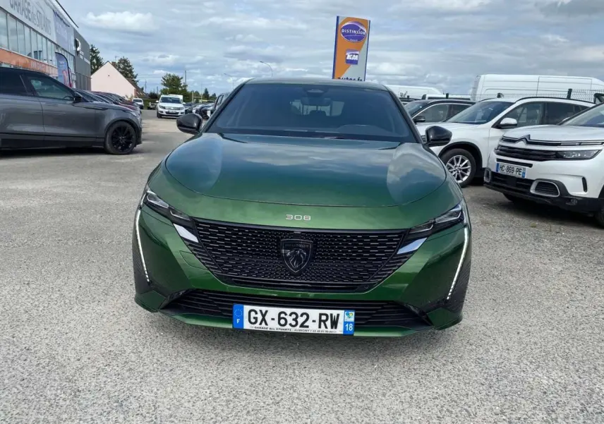 Vue avant d'une Peugeot 308 2023 vert olivine avec calandre noire et feux LED verticaux allumés.