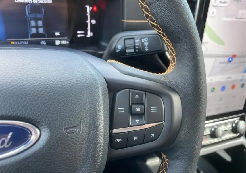 Gros plan sur le volant cuir noir avec surpiqûres orange du Ford Ranger Wildtrak 2025, affichage numérique et écran tactile visibles.