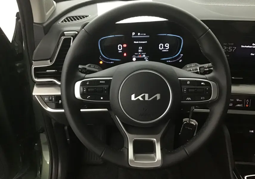 Vue rapprochée du volant noir du Kia Sportage 2025 vert Borneo, avec tableau de bord digital et commandes intégrées.