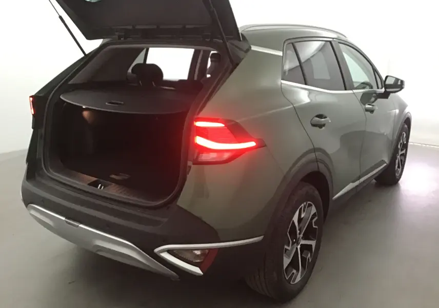 KIA SPORTAGE vert Borneo vu de trois quarts arrière droit avec coffre ouvert et feux arrière allumés.