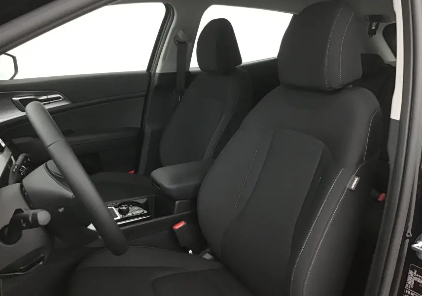 Intérieur avant du Kia Sportage 2025 avec sièges noirs et volant visible côté conducteur, ambiance sobre et moderne.