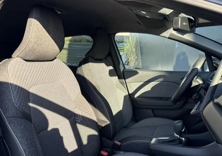 Vue intérieure côté conducteur du Renault Captur 2025, sièges tissu gris avec console centrale et volant textile.