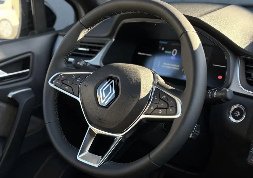 Vue rapprochée du volant noir avec logo Renault et tableau de bord numérique du Captur gris Rafale 2025.