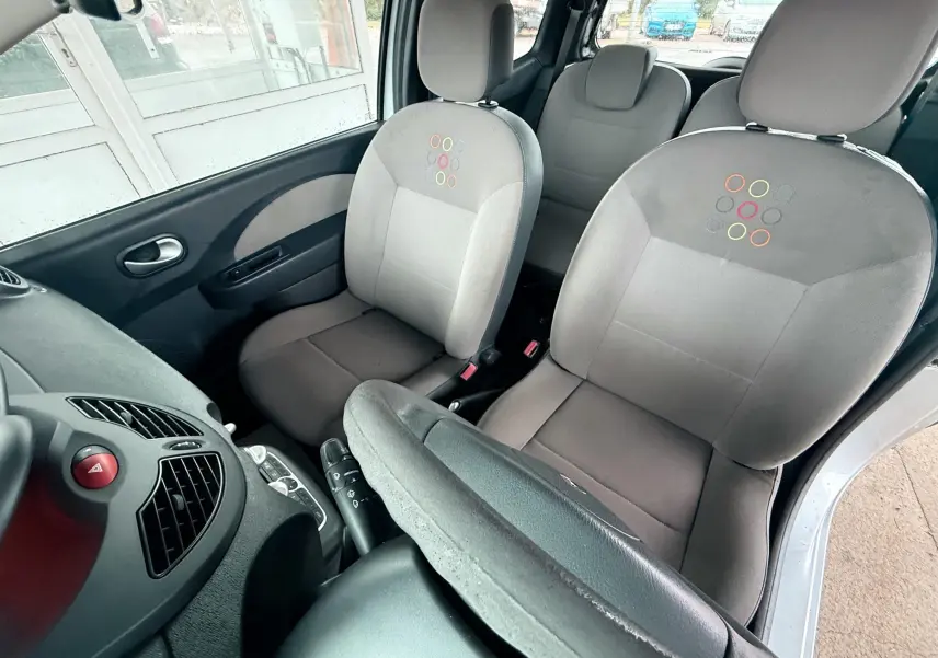 Vue intérieure avant droite de la Renault Twingo II 2009, sièges gris avec motifs colorés et volant cuir visible.