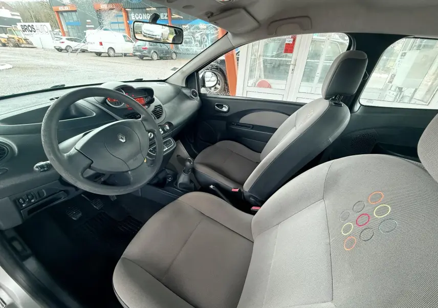 Vue intérieure côté conducteur de la Renault Twingo II 2009, sièges tissu gris avec motifs colorés et volant cuir noir.