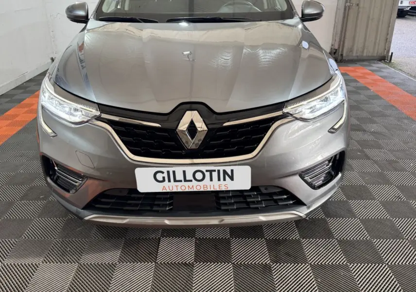 Vue avant rapprochée du Renault Arkana Business E-TECH 145 gris foncé avec phares LED allumés et calandre noire.