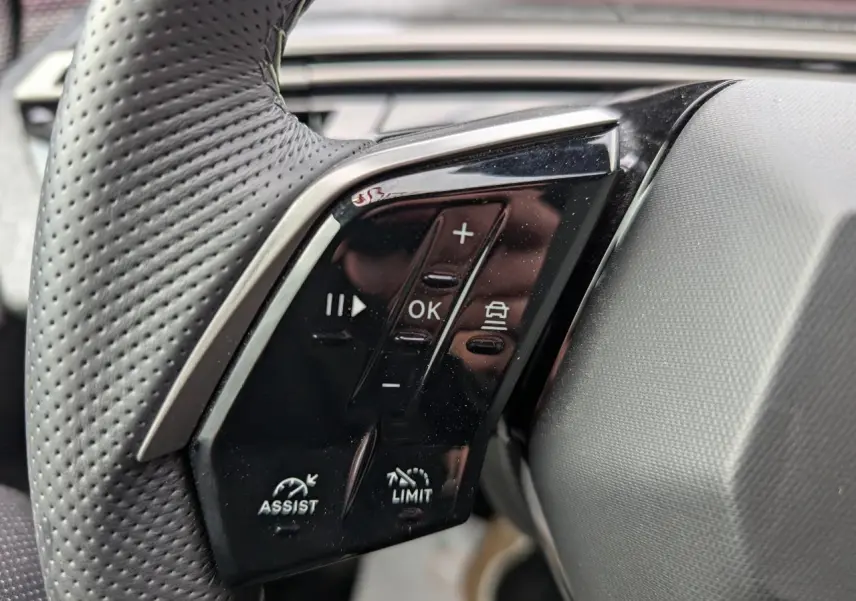Gros plan sur les commandes noires du volant perforé du Peugeot 3008 GT hybride 2025, côté gauche.