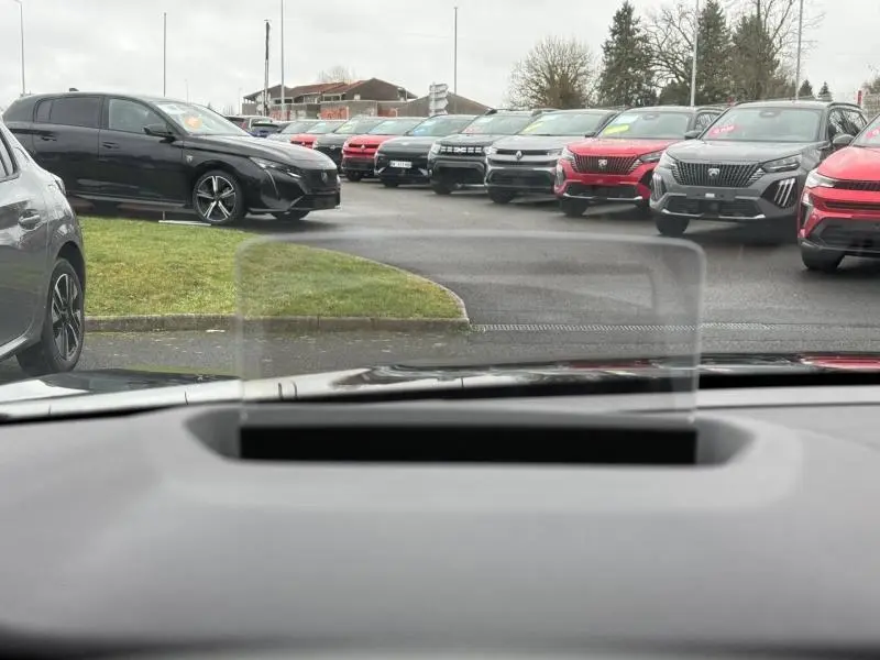 Vue depuis l'intérieur montrant une Citroën C4 X noire Perla Nera en 3/4 avant gauche sur un parking extérieur.