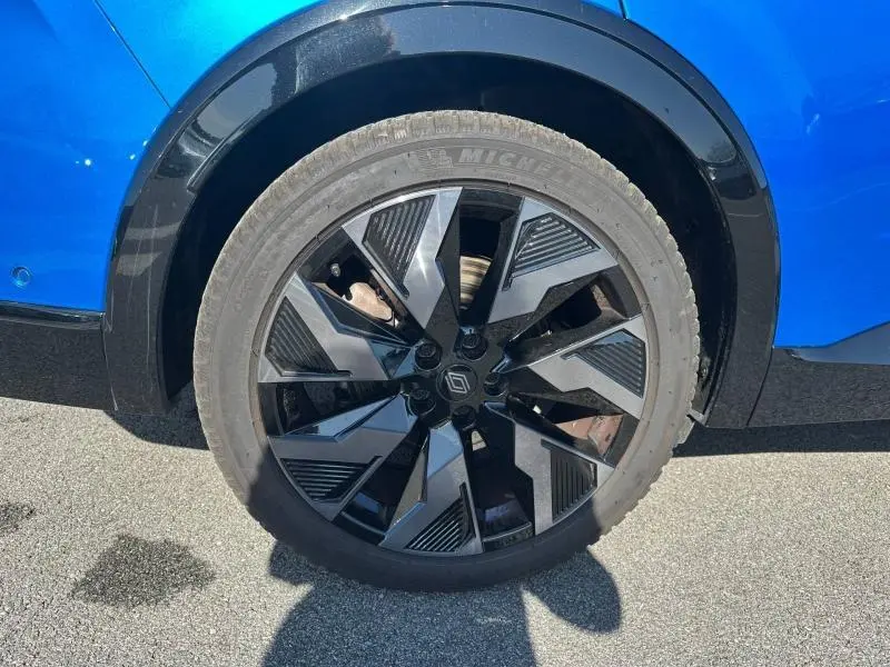 Gros plan sur la roue avant droite avec jante alu noire et détails géométriques du Renault Rafale Bleu Sommet métallisé.