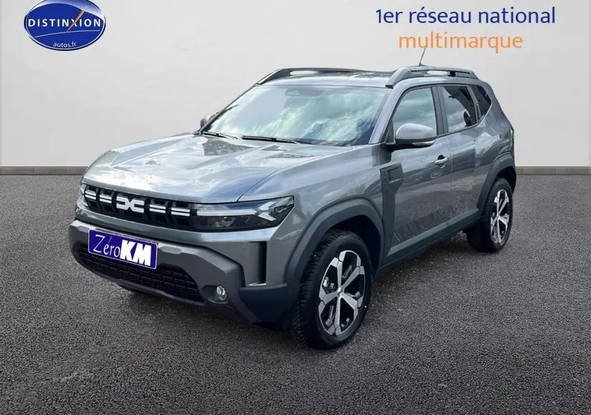 Dacia Duster gris schiste en 3/4 avant droit avec jantes alu et barres de toit visibles sur fond neutre.