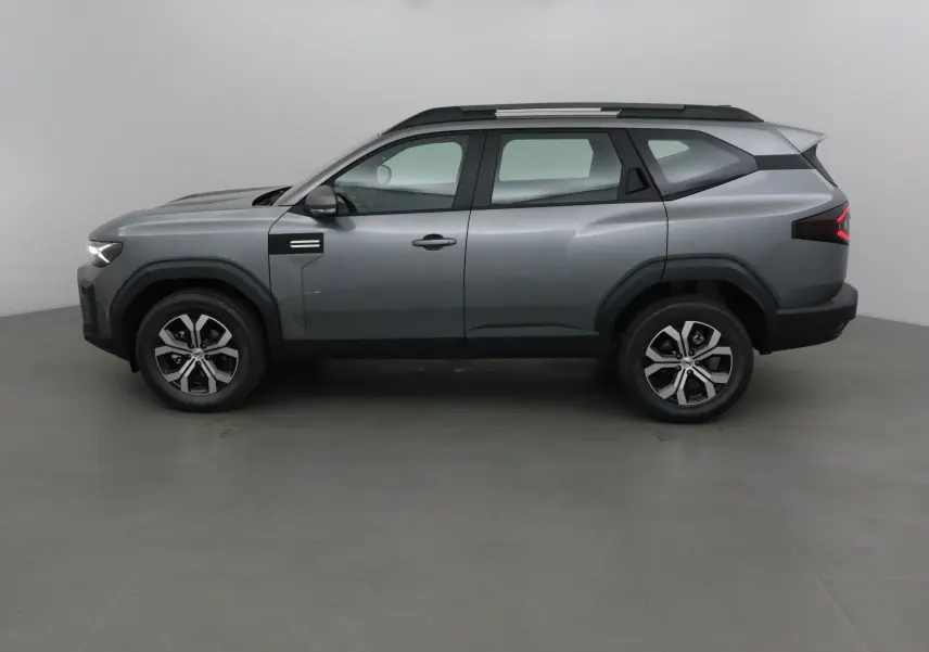 Profil droit du SUV Dacia Bigster gris schiste 2025 avec jantes alliage et barres de toit noires.