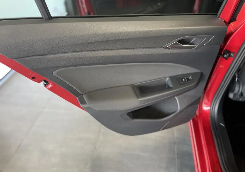 Porte arrière droite ouverte d'une Volkswagen Golf rouge métallisée, montrant le panneau intérieur gris foncé avec commande de vitre.