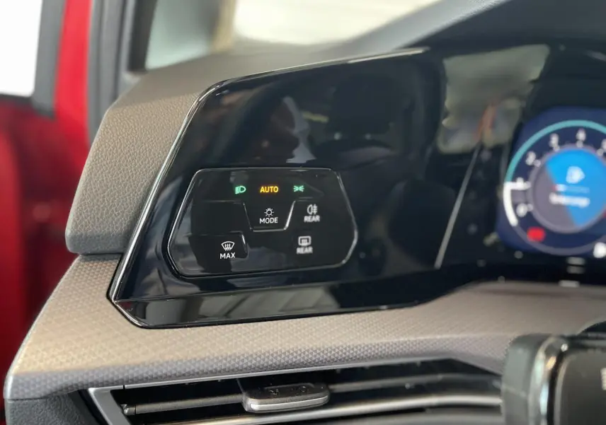 Panneau de commandes des feux et éclairages sur tableau de bord d'une Volkswagen Golf rouge métal, intérieur beige.