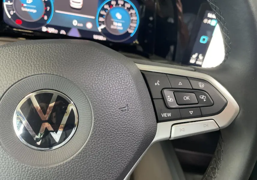 Gros plan sur le volant multifonction noir de la Volkswagen Golf 8 avec tableau de bord digital en arrière-plan.