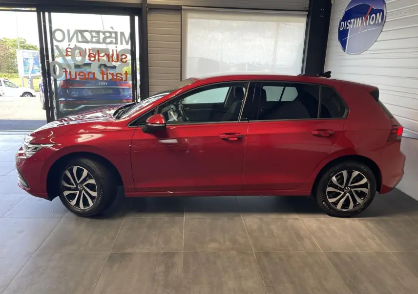 Profil droit d'une Volkswagen Golf rouge métal 2022 garée en intérieur avec jantes alliage distinctives.