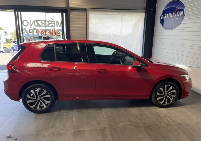 Profil côté gauche d'une Volkswagen Golf rouge métal 2022 avec jantes alliage et vitres teintées en showroom.