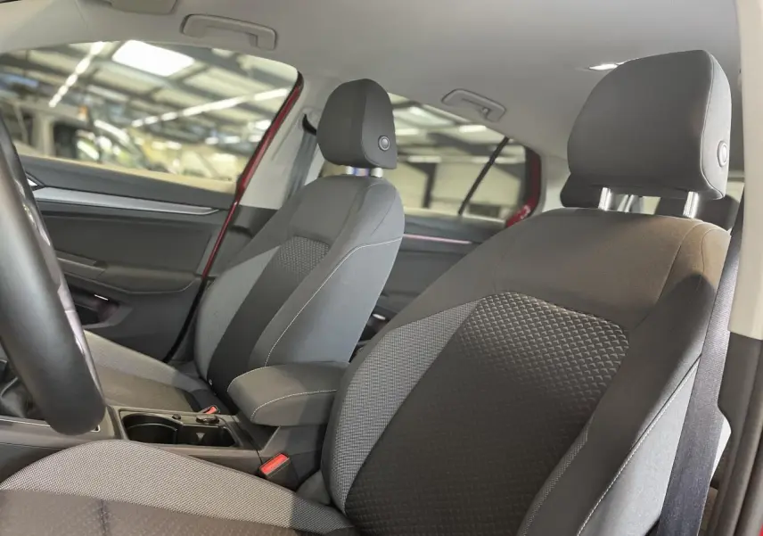 Intérieur avant de la Volkswagen Golf rouge métal 2022, sièges tissu Waveform gris et noir avec accoudoir central.