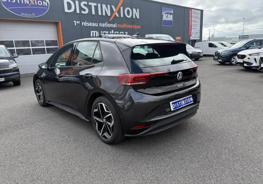 Vue 3/4 arrière droite d'une Volkswagen ID.3 Pro S gris manganese avec toit noir, stationnée devant un concessionnaire.