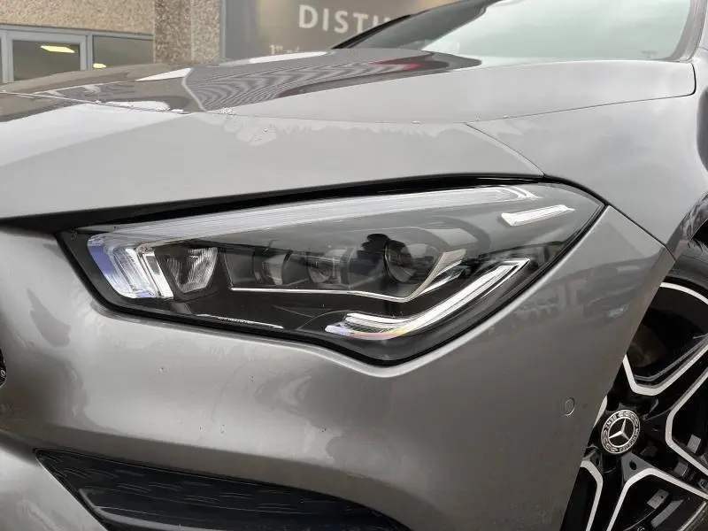 Gros plan sur le phare avant droit gris montagne métallisé d'une Mercedes CLA Shooting Brake AMG Line 2022.