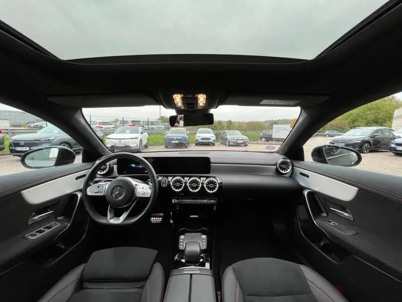 Vue intérieure frontale du poste de conduite de la Mercedes CLA Shooting Brake 250 AMG Line, avec toit ouvrant panoramique et finitions aluminium.