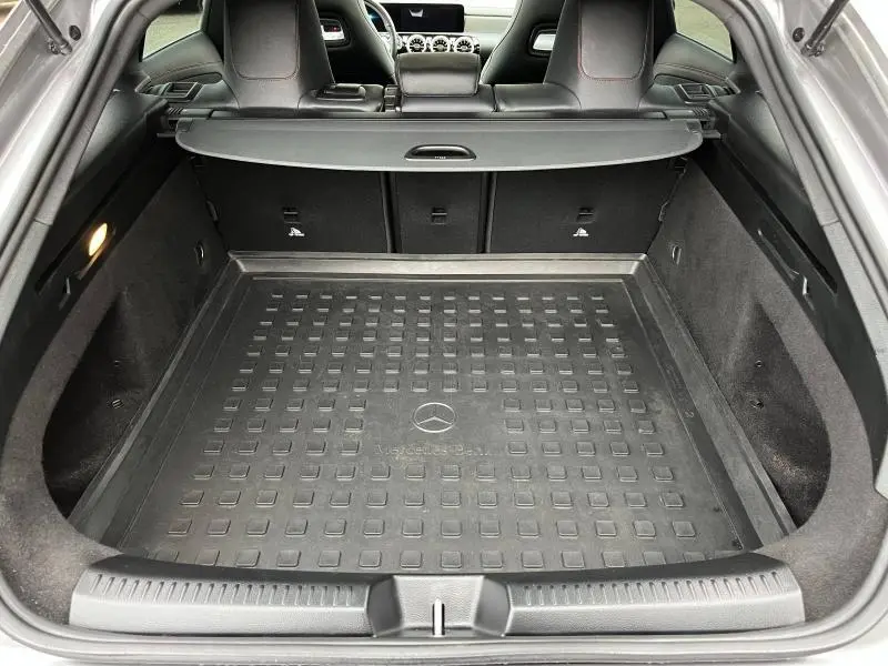 Coffre ouvert vu de l'arrière d'une Mercedes CLA Shooting Brake gris montagne, avec tapis de coffre noir et filet de séparation.