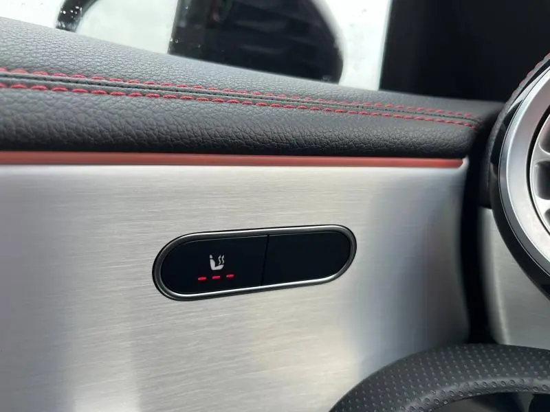 Détail du bouton de siège chauffant sur la garniture alu brossé avec surpiqûres rouges dans une Mercedes CLA Shooting Brake 250 AMG Line.