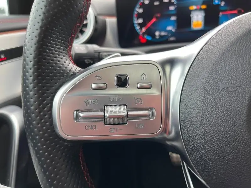 Gros plan sur le volant cuir noir perforé côté gauche avec commandes argentées du Mercedes CLA Shooting Brake gris montagne métallisé 2022.