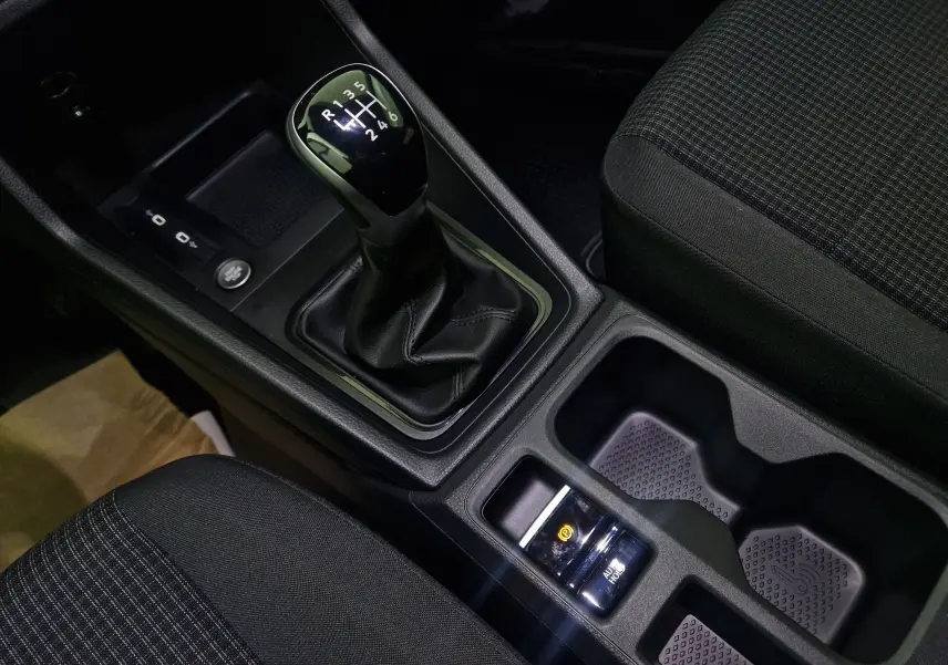 Gros plan sur la console centrale noire du Volkswagen Caddy Maxi blanc, montrant le levier de vitesse manuel et les porte-gobelets.