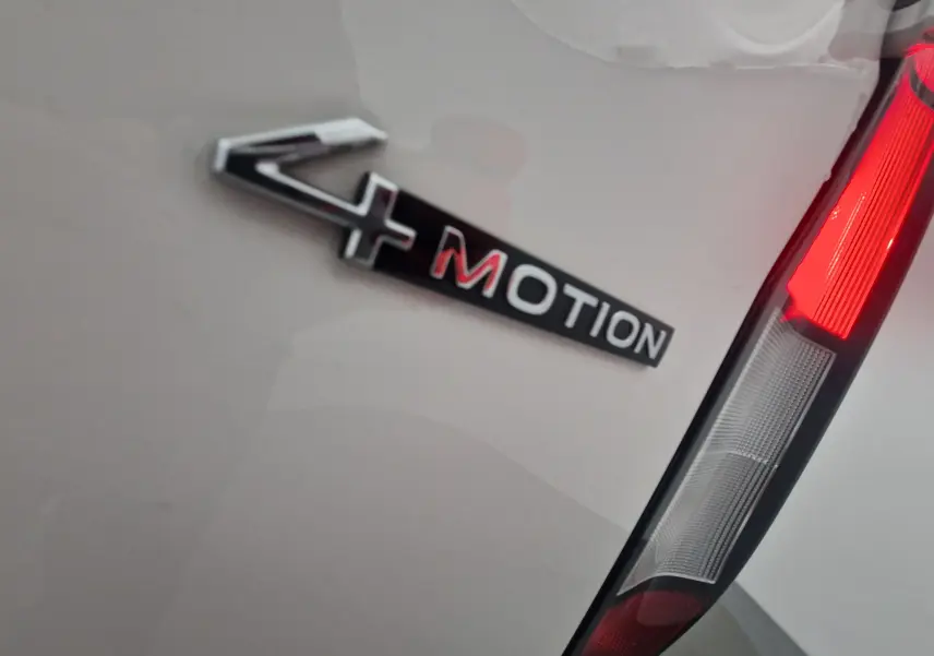 Gros plan sur l'emblème 4MOTION et le feu arrière droit d'un Volkswagen Caddy Maxi blanc.