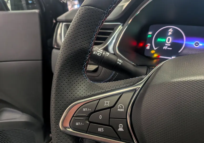 Gros plan sur le volant en cuir perforé noir du Renault Captur E-Tech 2025, avec commandes intégrées et tableau de bord numérique lumineux.