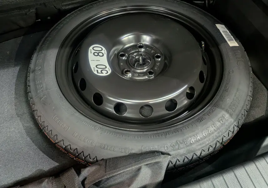 Roue de secours noire en acier avec étiquette de limitation de vitesse, dans le coffre d'un Renault Captur E-TECH 2025 noir étoilé.