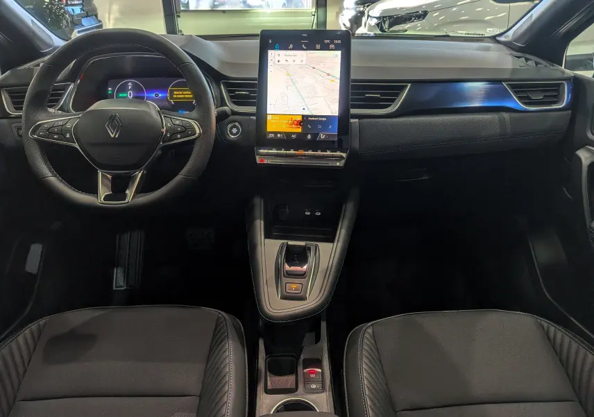 Vue intérieure du tableau de bord et volant du Renault Captur E-TECH 2025 avec écran tactile central et sellerie noire.