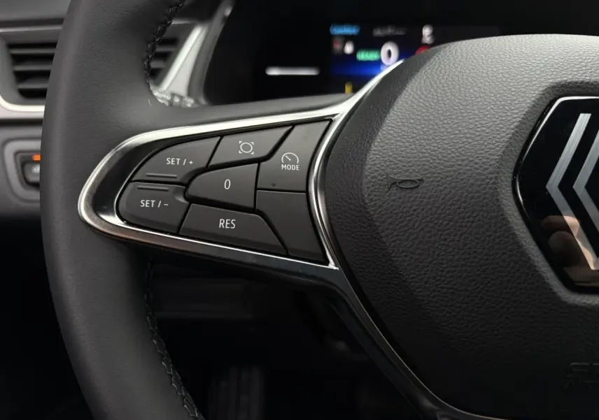 Gros plan sur les commandes à gauche du volant noir du Renault Captur 2025 hybride, avec logo Renault visible.