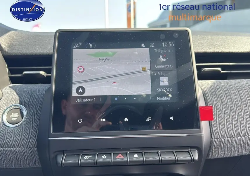 Vue intérieure centrée sur l'écran tactile du tableau de bord de la Renault Clio V noire, avec bouton start engine visible à gauche.