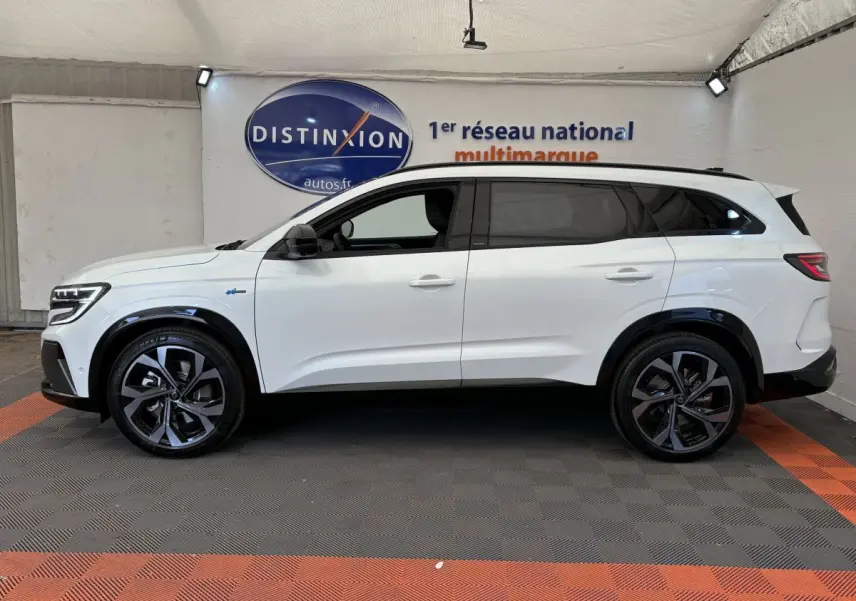 Profil droit d’un Renault Espace blanc esprit Alpine 7 places, avec jantes noires et vitres teintées, en intérieur showroom.