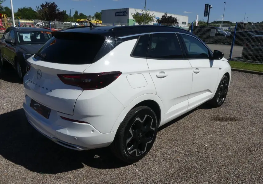 Opel Grandland blanc métallisé en vue 3/4 arrière droit avec toit noir brillant et jantes noires.