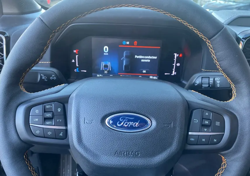 Vue rapprochée du volant cuir noir avec surpiqûres orange et tableau de bord numérique du Ford Ranger gris carbone 2026.