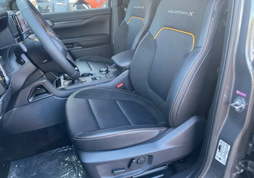 Vue intérieure côté conducteur du Ford Ranger 205 Wildtrak X gris carbone, sièges en cuir noir avec surpiqûres orange et logo Wildtrak X brodé.