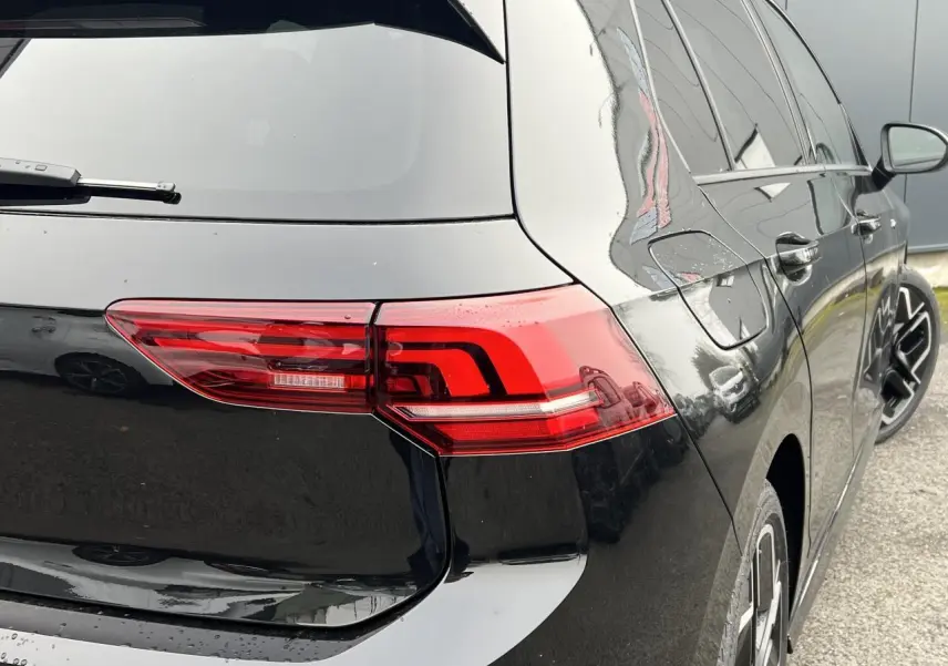 Vue 3/4 arrière droite d'une Volkswagen Golf VIII noire avec feux arrière LED et jantes alliage 18 pouces.