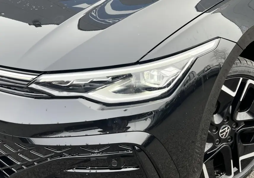 Gros plan sur l'avant droit noir brillant d'une Volkswagen Golf VIII R-Line, mettant en valeur le phare LED et la jante alliage 18 pouces.