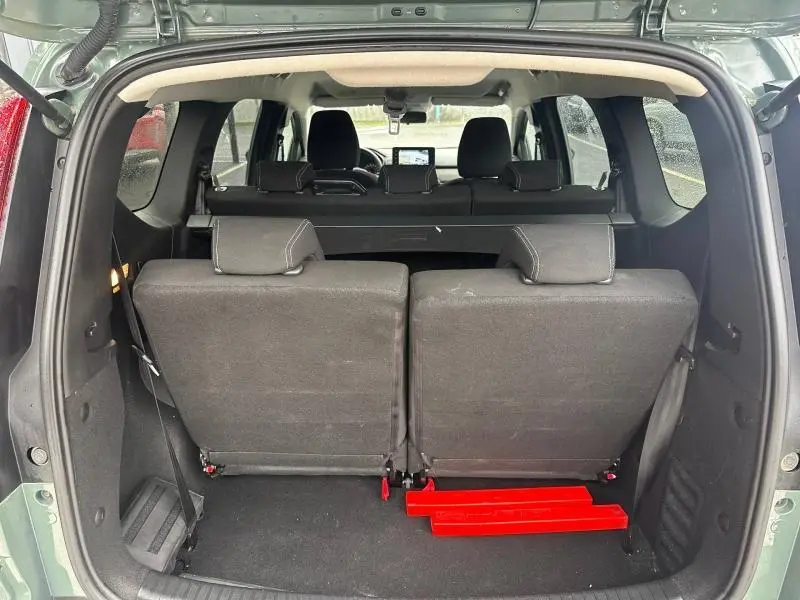 Vue arrière du coffre ouvert du Dacia Jogger 2025 Kaki Lichen, montrant les sièges arrière et un triangle de sécurité rouge.