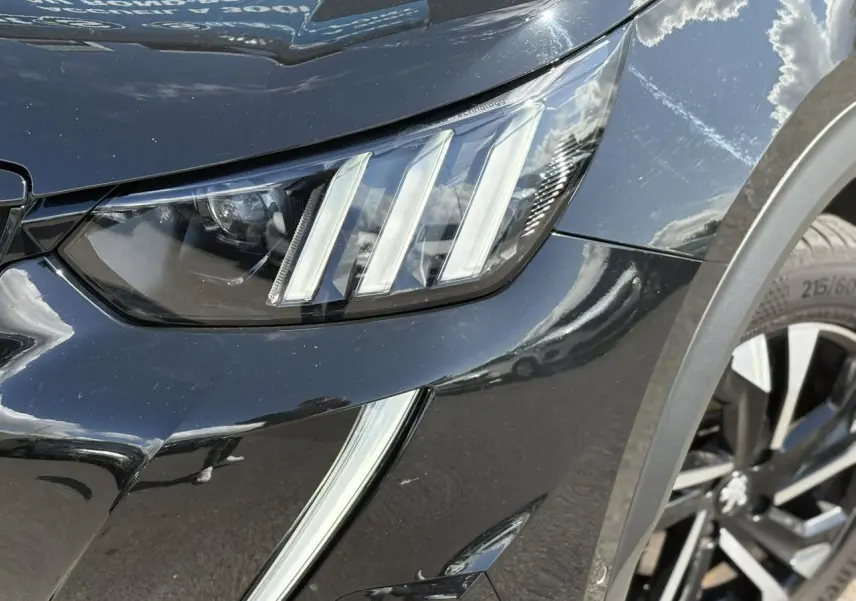Gros plan sur le phare avant gauche et jante alliage bi-ton du Peugeot 2008 noir Onyx finition GT.