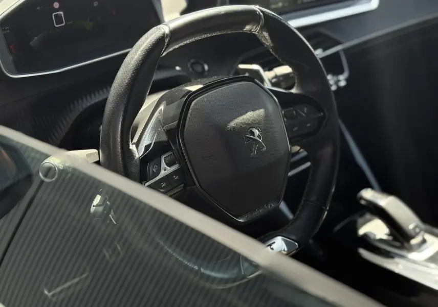 Vue rapprochée du volant cuir noir avec logo Peugeot du 2008 GT, montrant aussi la console centrale et levier de vitesse.