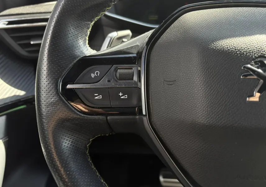 Gros plan sur le côté gauche du volant cuir noir du Peugeot 2008 GT avec surpiqûres vertes et commandes multimédia intégrées.