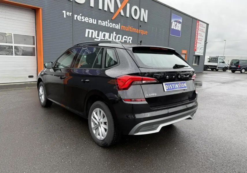 Vue 3/4 arrière droite d'un Skoda Kamiq noir Magic nacré avec feux arrière LED et jantes argentées, stationné devant un bâtiment.