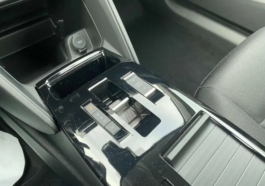 Gros plan sur la console centrale noire brillante de la Citroën C4 hybride 2025 avec sélecteur de boîte auto et bouton Drive Mode.
