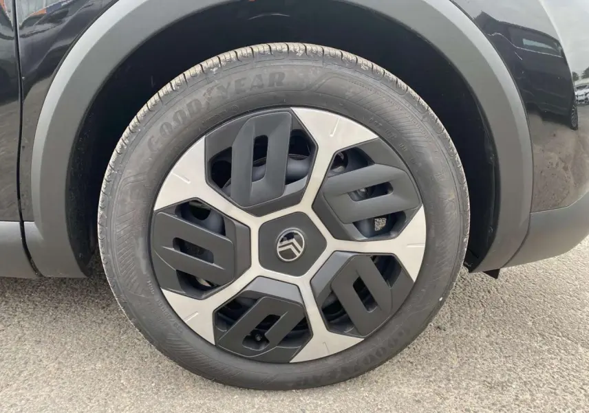 Gros plan sur la roue avant gauche noire Perla Nera d'une Citroën C4 hybride avec jante au design géométrique bicolore.