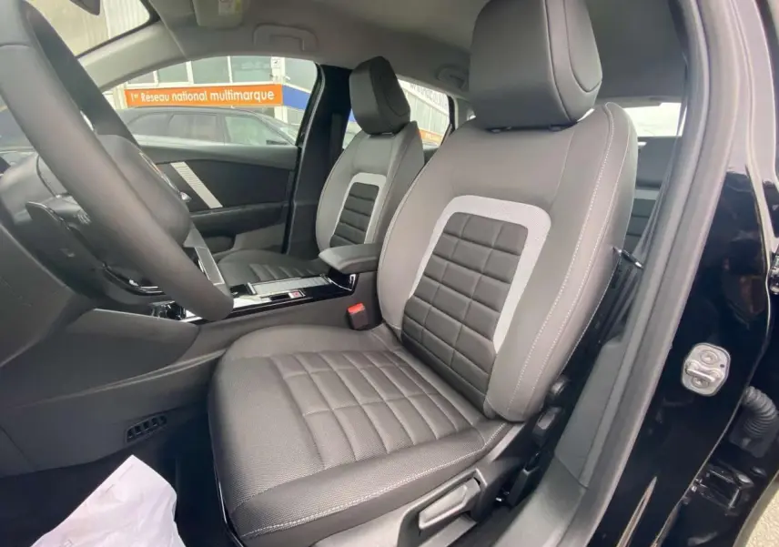 Intérieur de la Citroën C4 hybride 2025 vue côté conducteur, sièges gris avec surpiqûres blanches, porte noire ouverte.